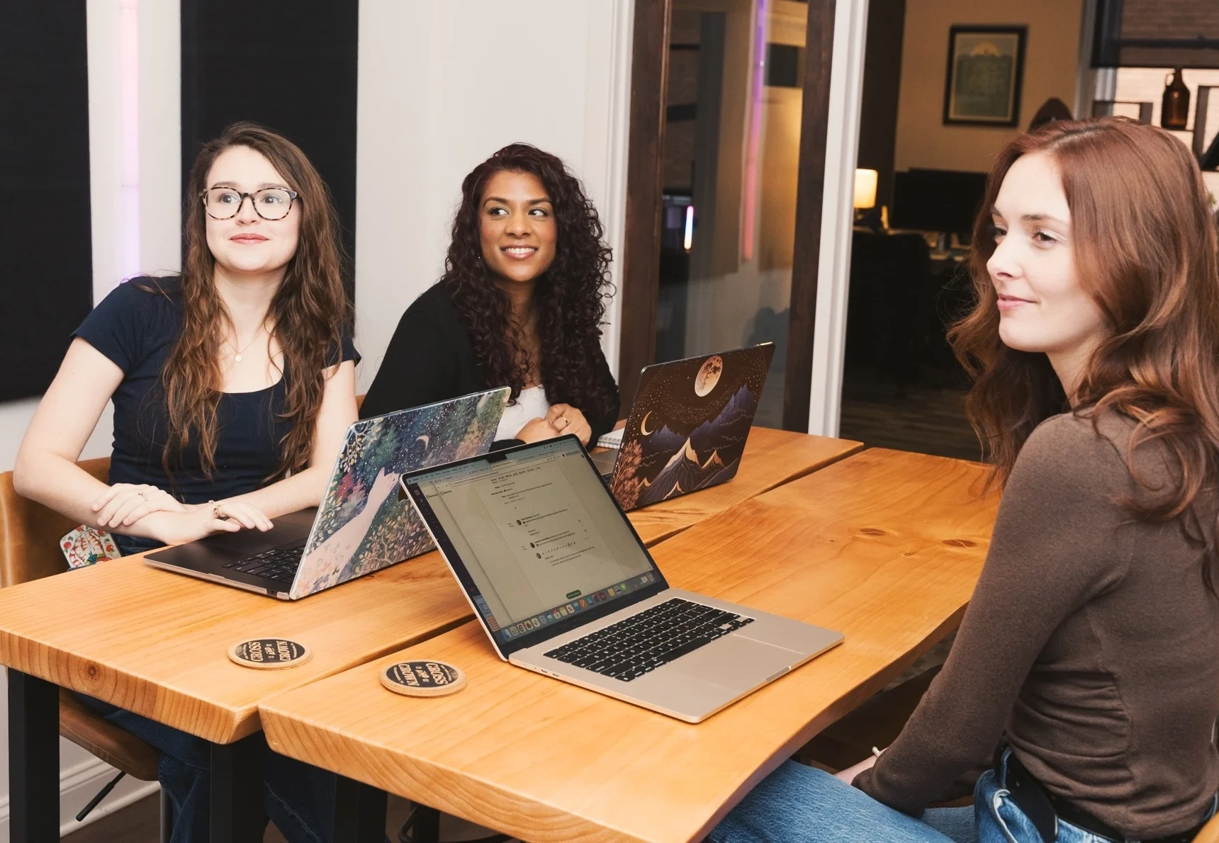 3 Cross & Crown employees looking to the side, sitting around a table with laptops