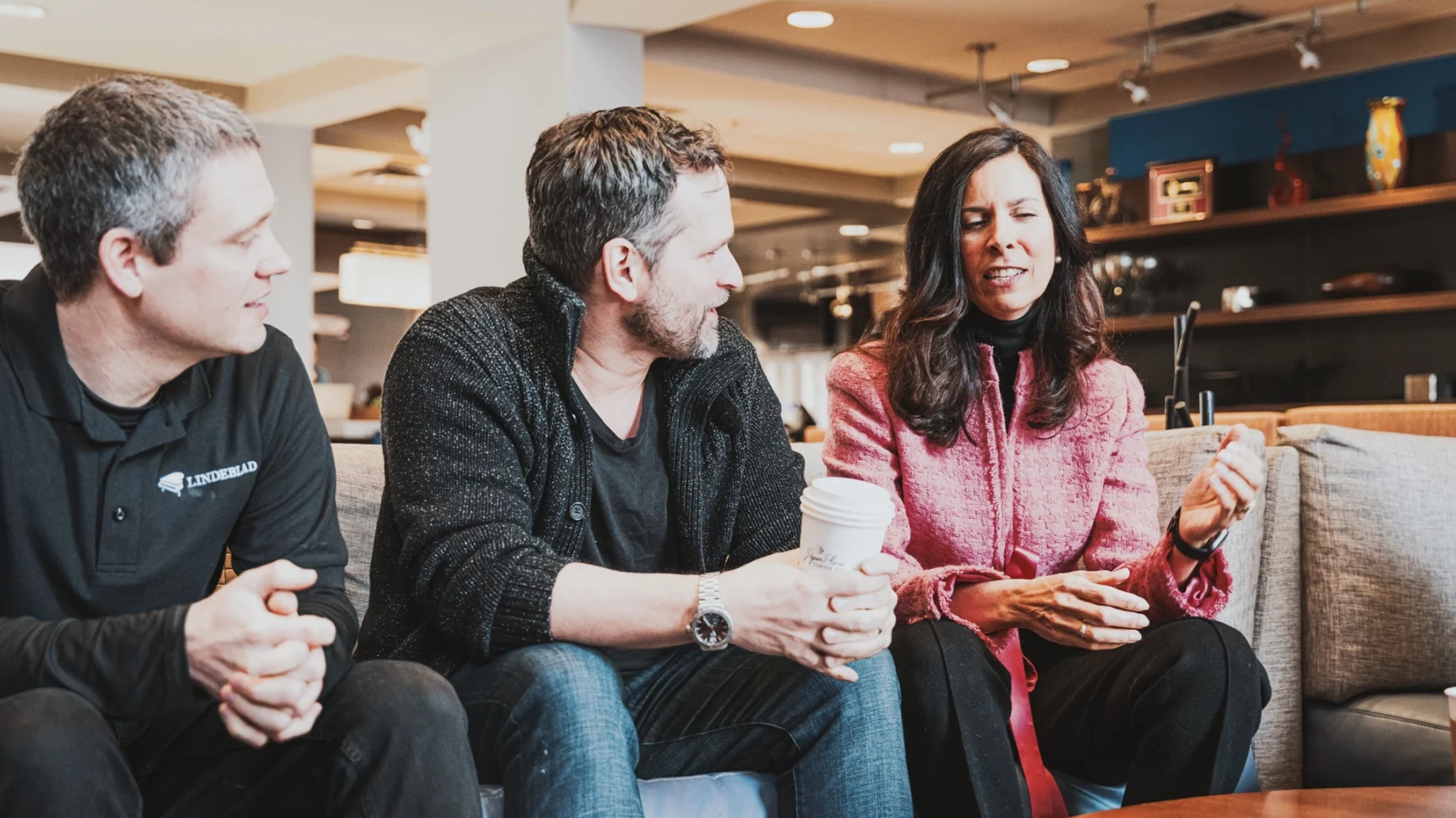 Three C12 members sitting on a couch talking in a hotel lobby with coffee.