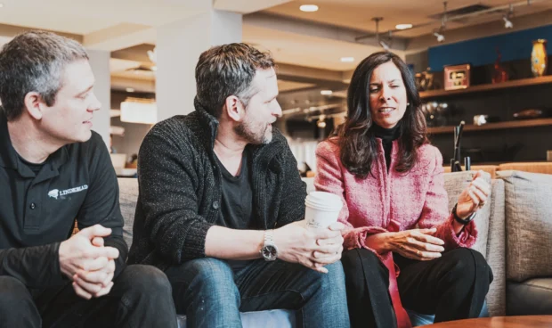 Three C12 members sitting on a couch talking in a hotel lobby with coffee.