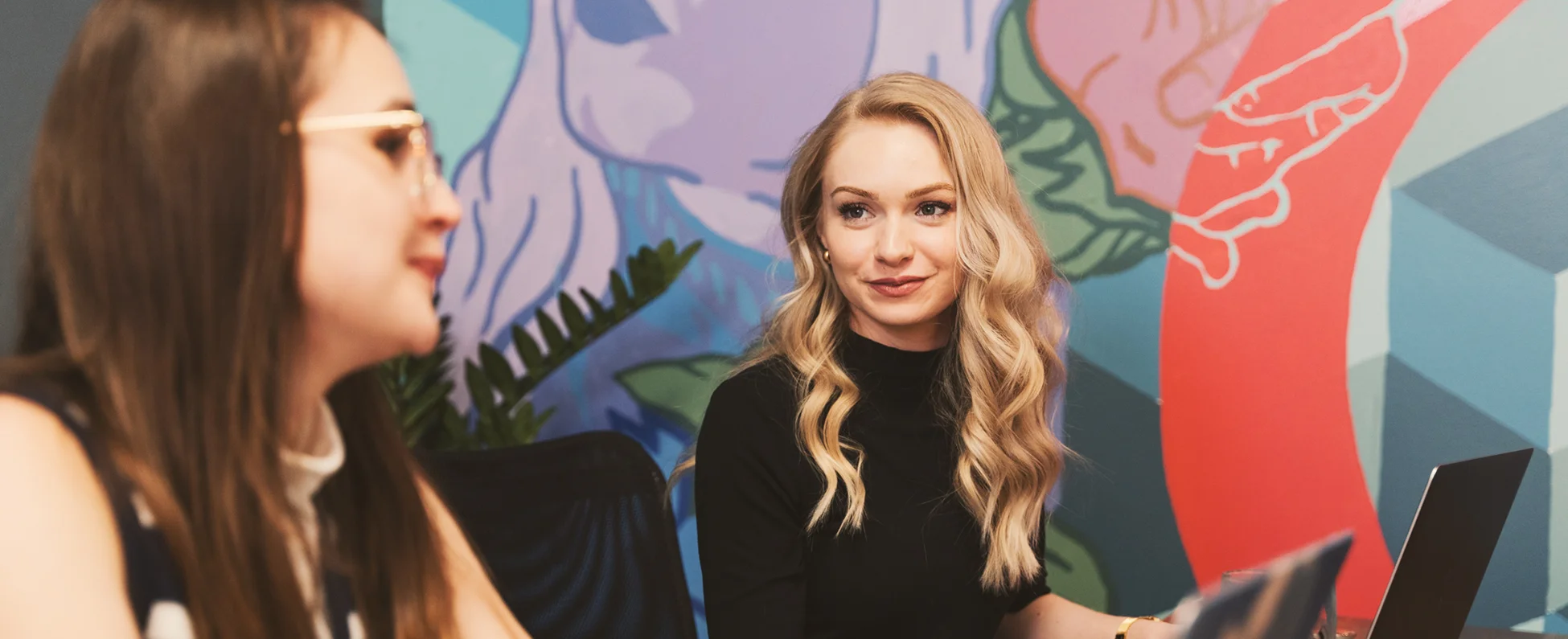 Digital Marketing Team meeting featuring Ali and Rachel with a colorful mural in the background.
