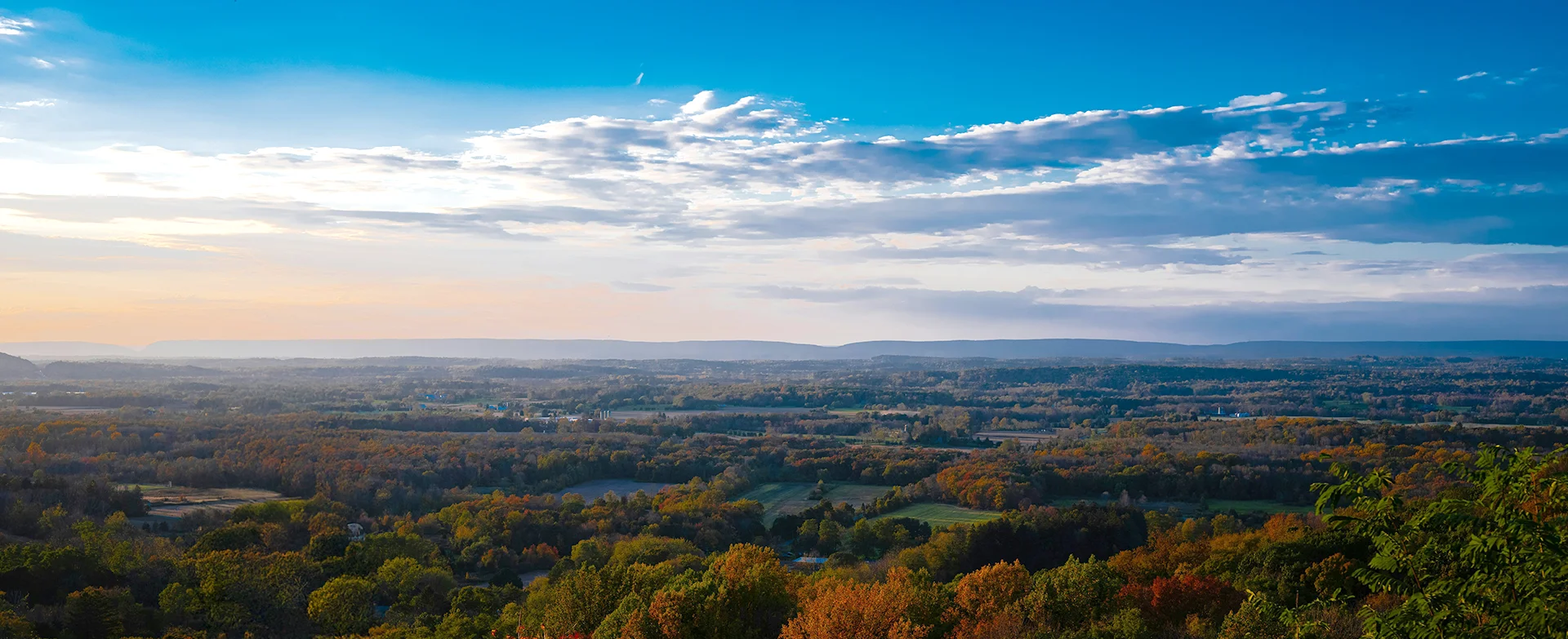 Natural Lands overlook landscape during sunrise, featuring lots of trees and clouds.