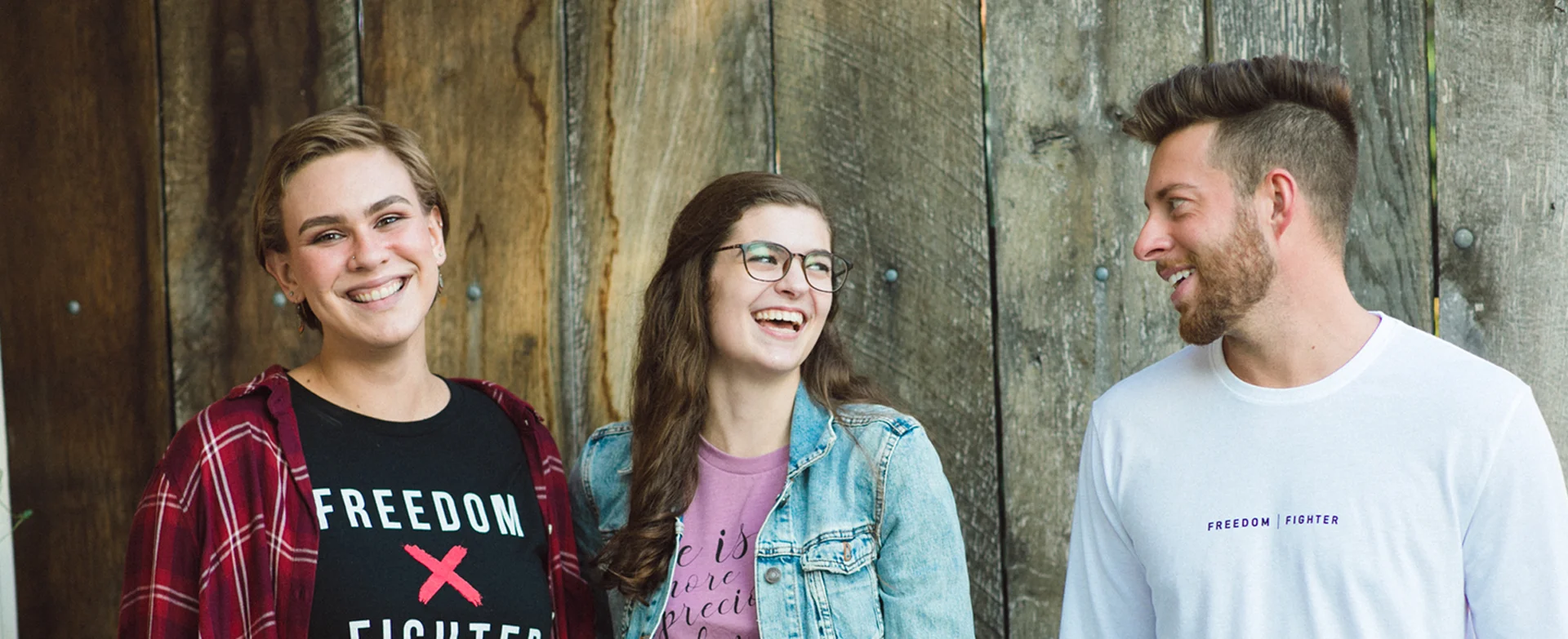 Three people smiling in front of a wooden wall.