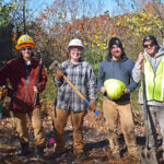 6 people standing next to each other in a wooded area.
