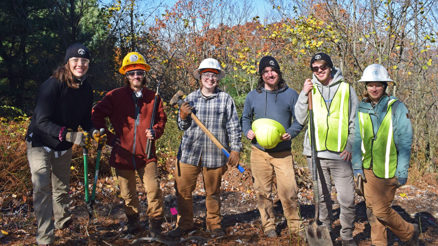 6 people standing next to each other in a wooded area.