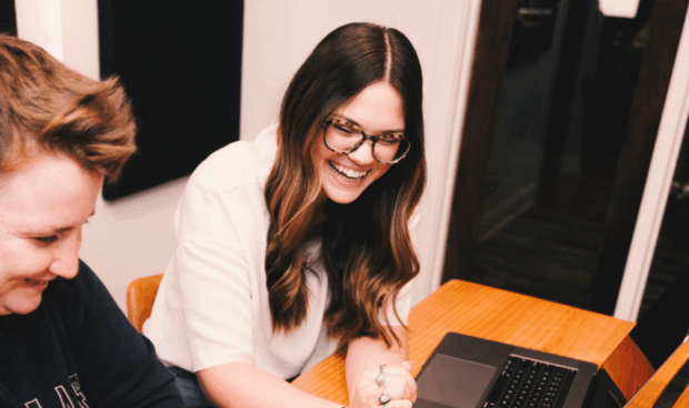 two people sitting at a table with laptops