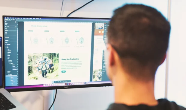 A person looks at a computer screen displaying a website with images of people hiking and text about graphics