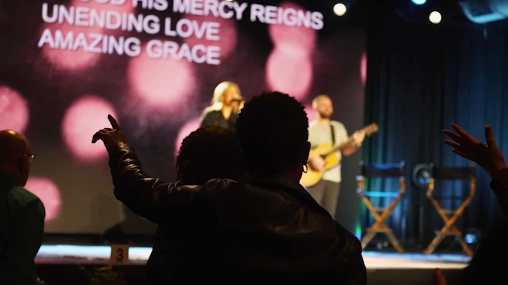 A screen displays the words "UNENDING LOVE AMAZING GRACE" as a band performs on stage with a guitarist and singer.