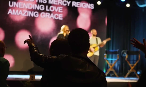 A screen displays the words "UNENDING LOVE AMAZING GRACE" as a band performs on stage with a guitarist and singer.