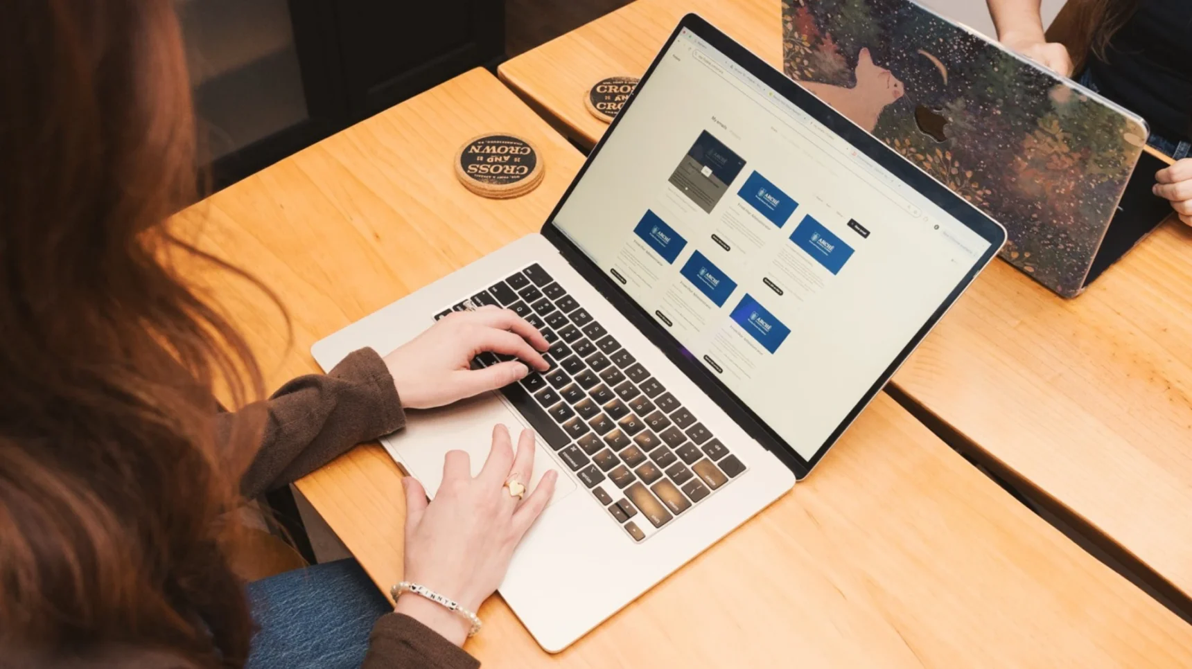 A person is typing on a laptop with a website displayed on the screen. Another laptop is open next to it.