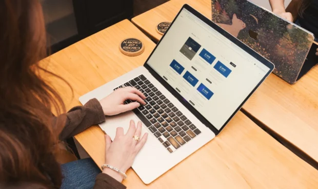 A person is typing on a laptop with a website displayed on the screen. Another laptop is open next to it.