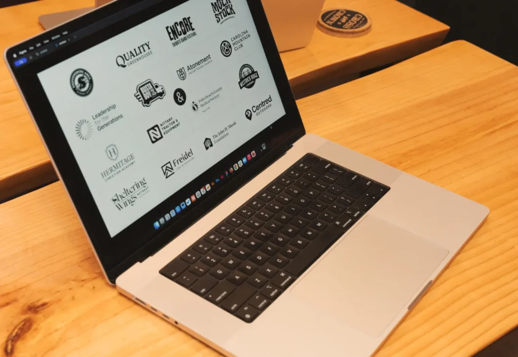 A laptop open on a wooden desk displays a screen filled with various black and white logos.