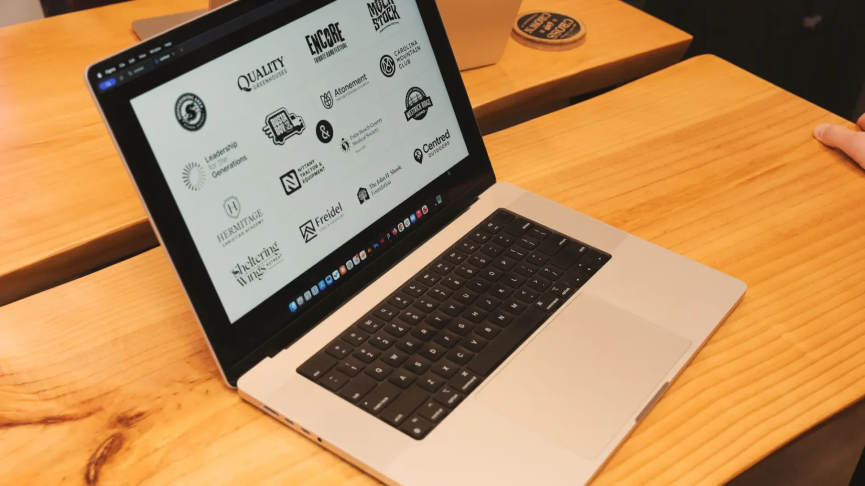 A laptop open on a wooden desk displays a screen filled with various black and white logos.