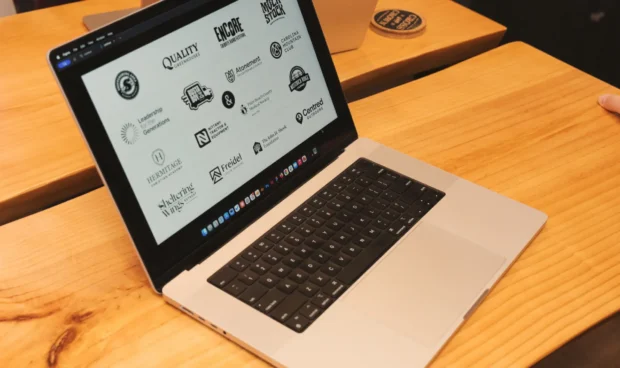A laptop open on a wooden desk displays a screen filled with various black and white logos.