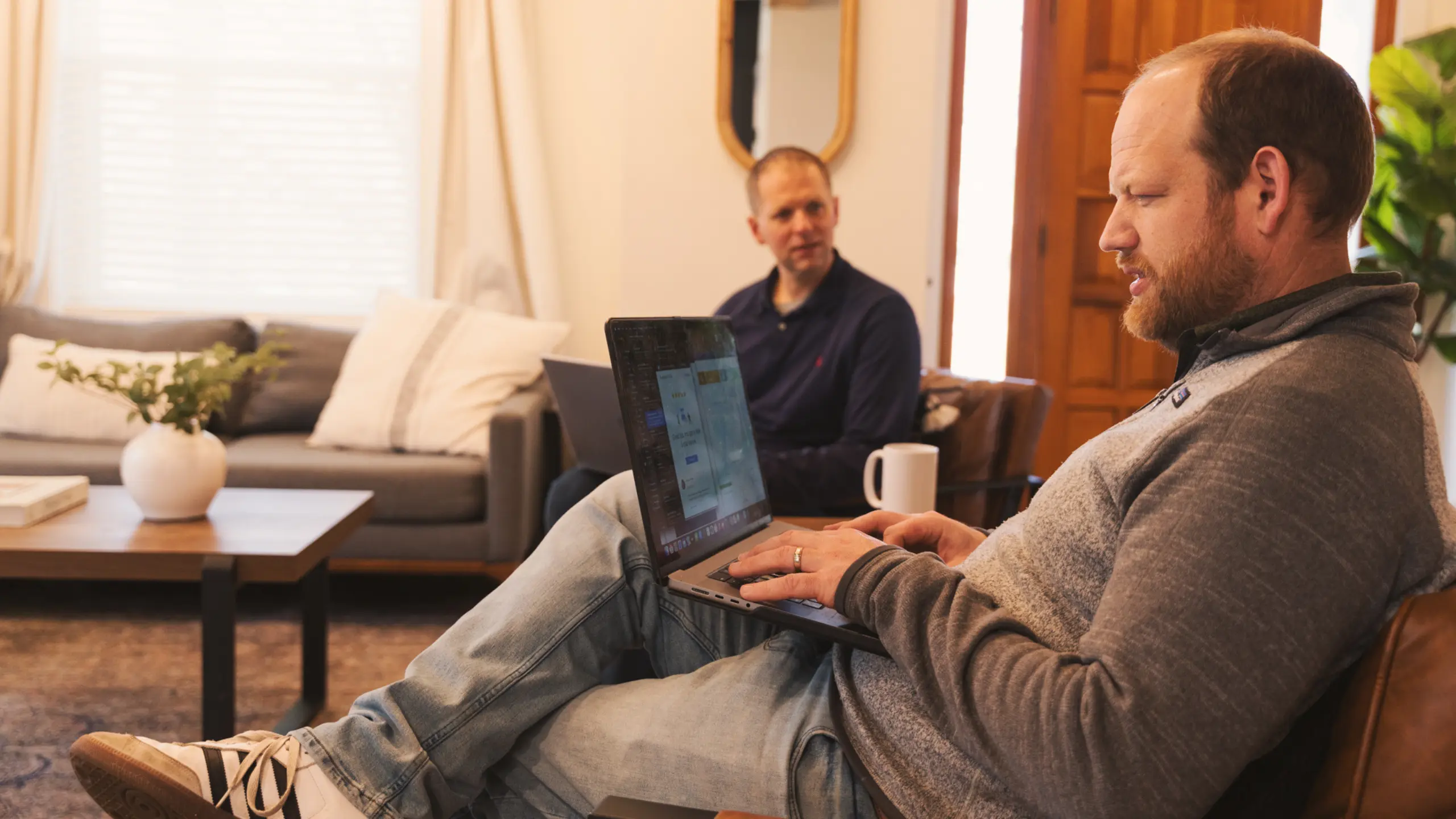 Two people collaborate on a laptop computer on a wooden table. One person's hands are on the keyboard, while the other person's hands are near the trackpad.